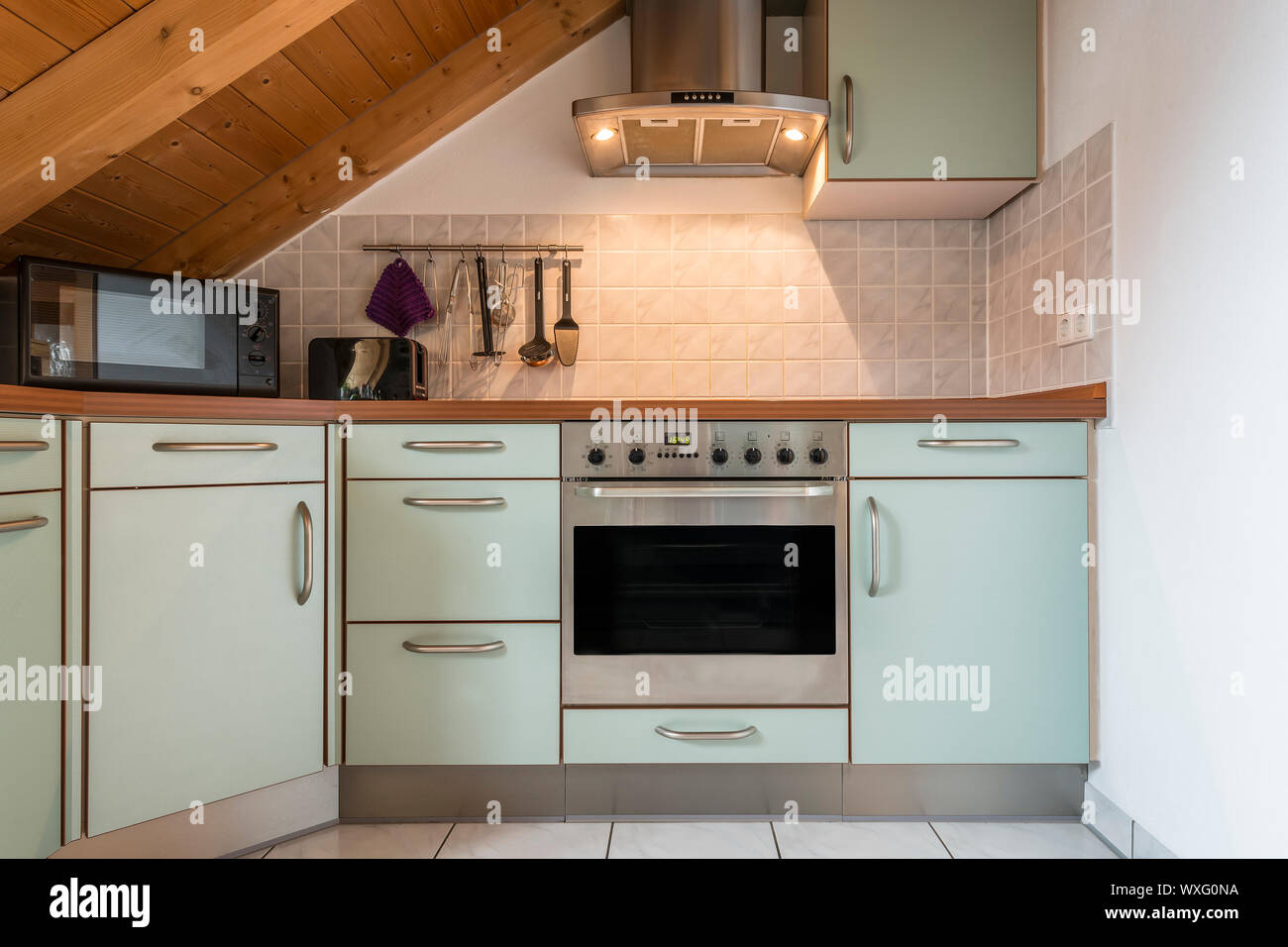 kitchen of a flat with oven, microwave, stove, hood, cabinets and wooden ceiling Stock Photo