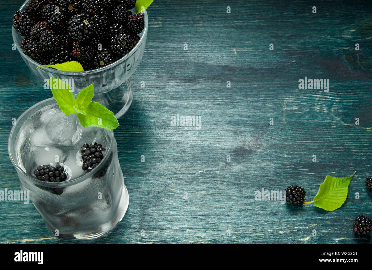 Fresh blackberry. Juicy blackberry in a bowl and a glass of cold ice water with berries on a wooden table. View from above. Copy Stock Photo