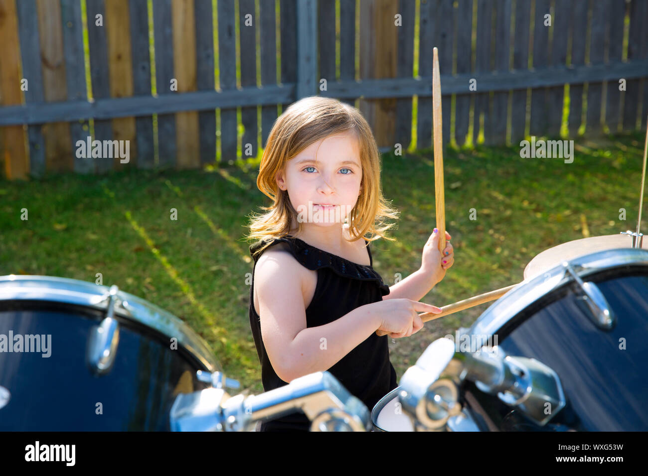 Drummer blond kid girl playing drums in tha backyard lawn Stock Photo