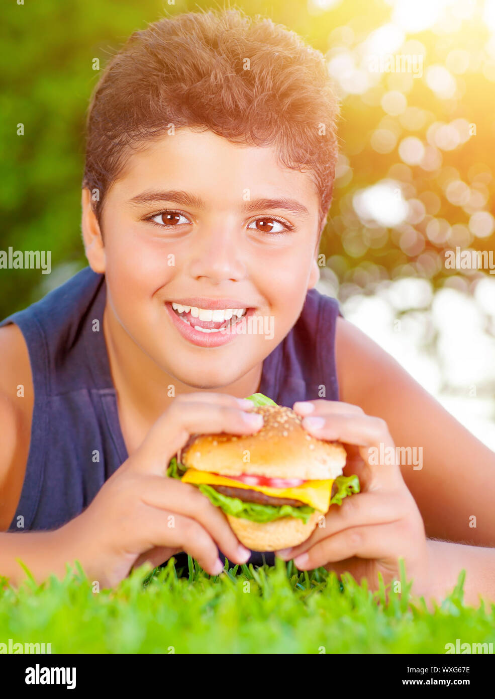 Closeup portrait of cute arabic boy eating burger outdoors, lying down on  green grass and enjoying picnic in the park in summer, happy childhood  conce Stock Photo - Alamy