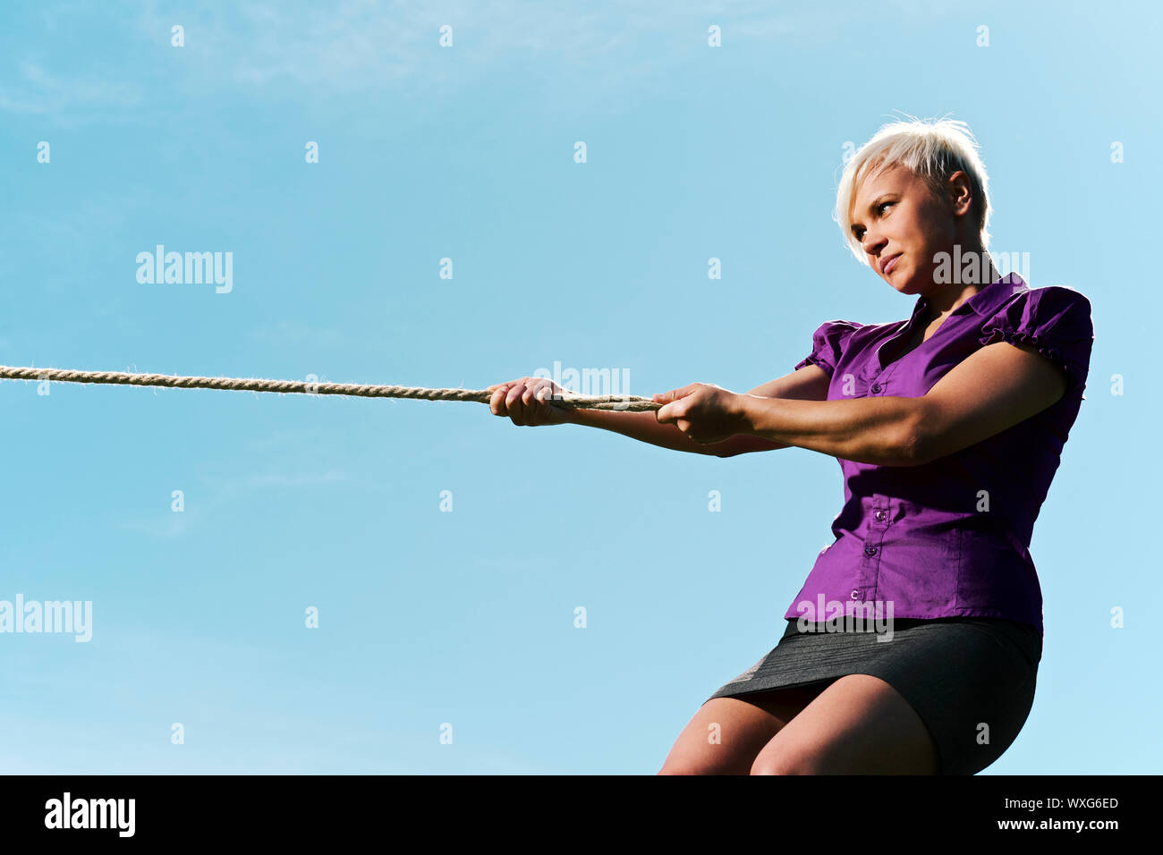 resolute business woman pulling rope against blue sky, symbol of power ...