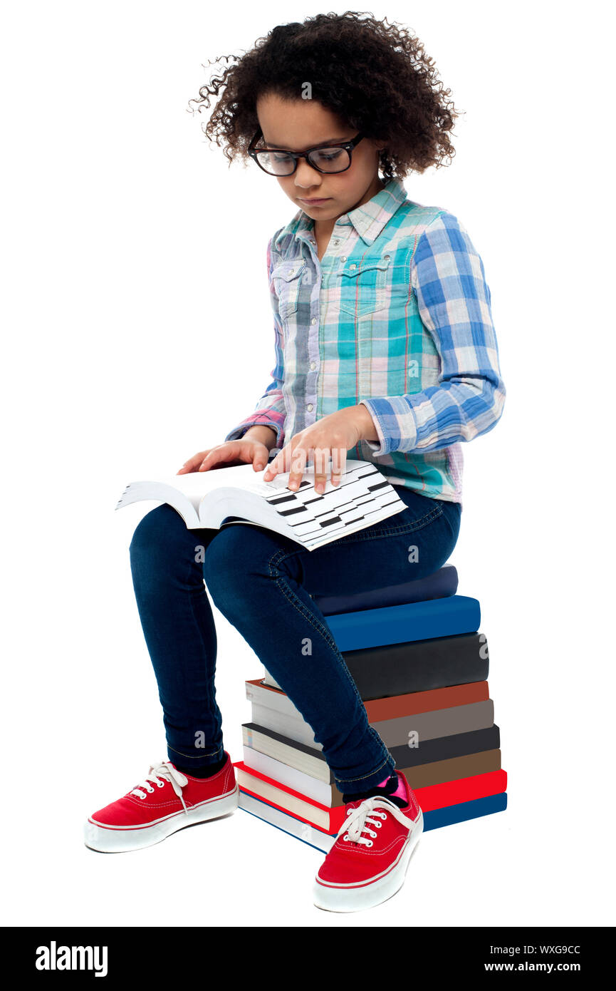 Kid wearing spectacles sitting on stack of books and learning Stock