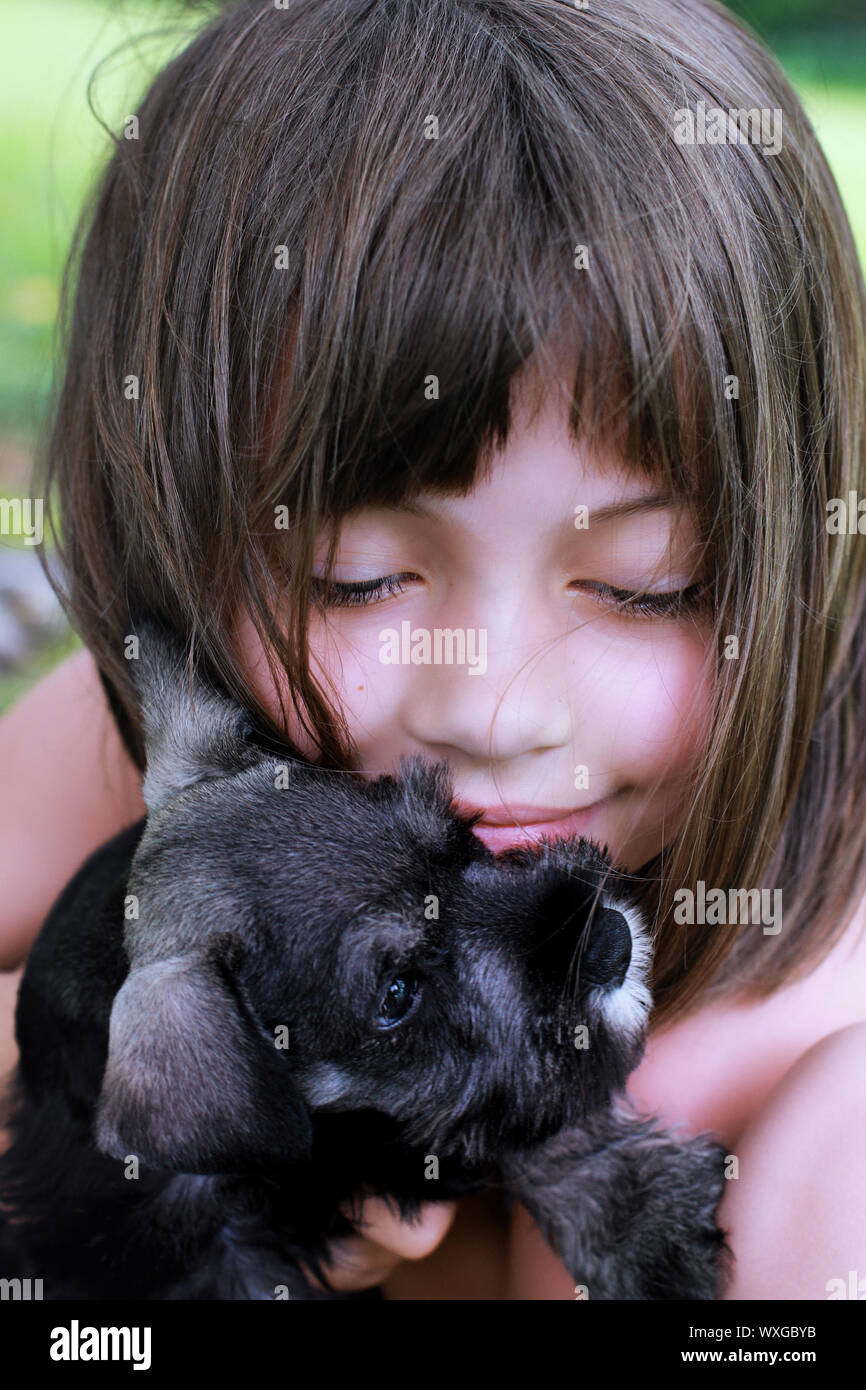 Little girl hugging her Mini Schnauzer puppy. Extreme shallow depth of field with selective focus on child's face. Stock Photo
