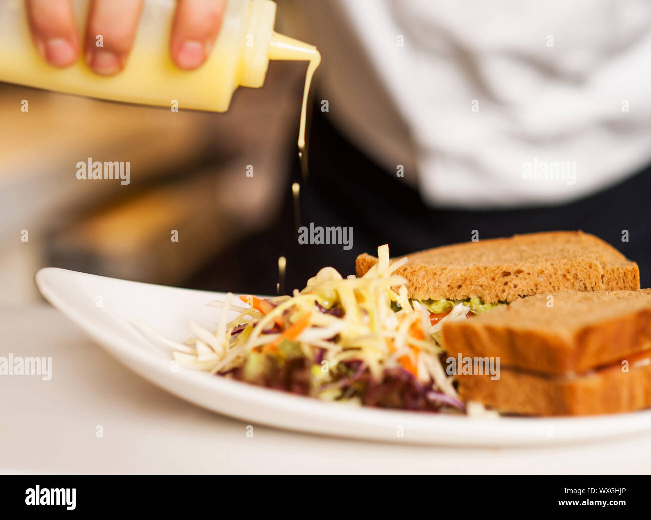 Chef pouring mayonnaise sauce on the vegetable salad with brown bread