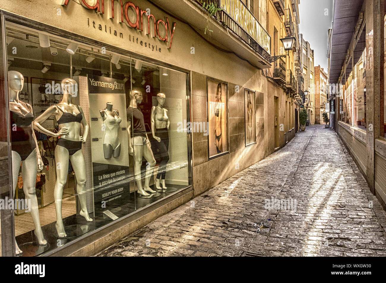 A cobble stone street in Seville, Spain, flanked by store fronts featuring high end clothes