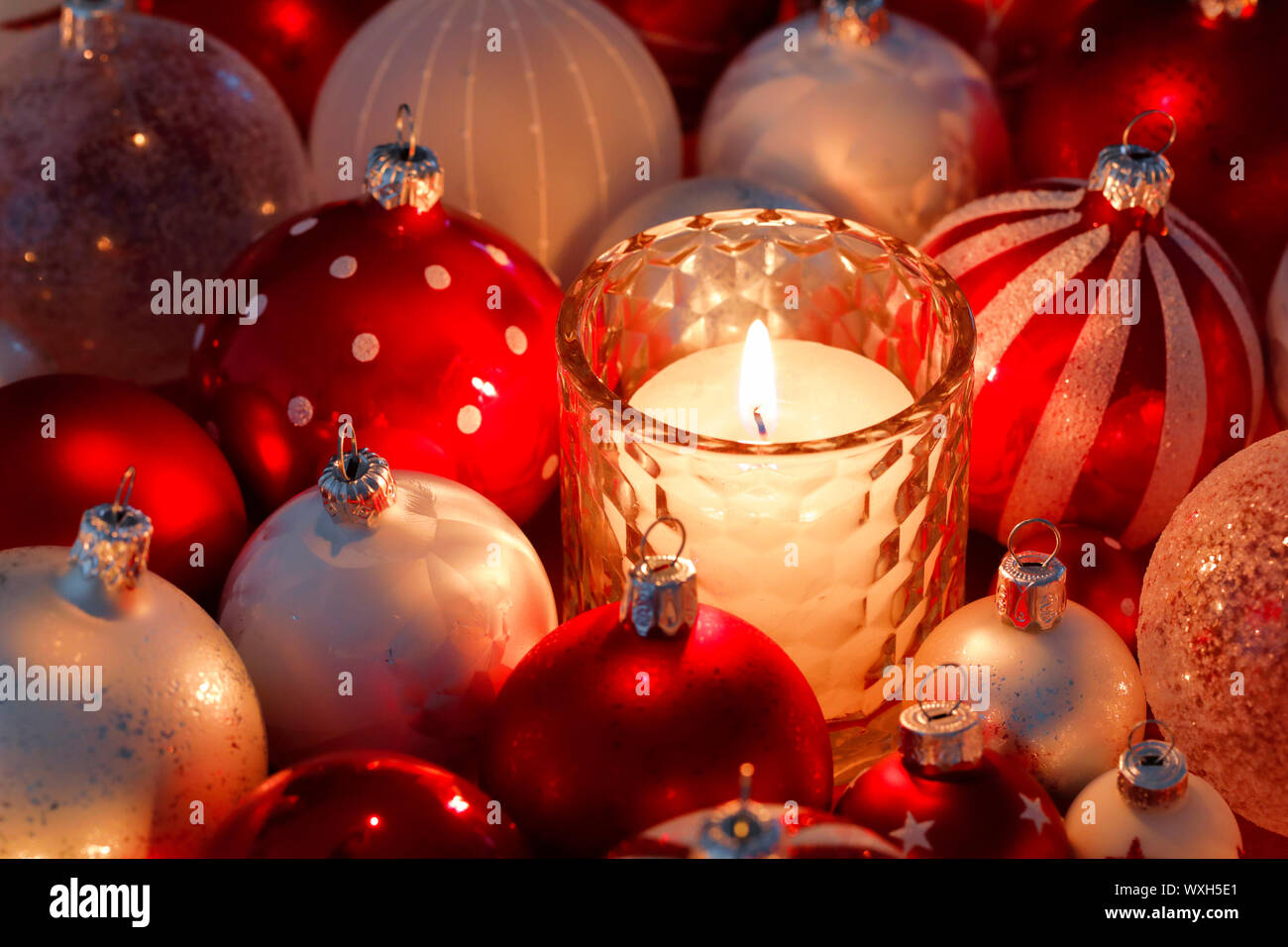 Christmas decoration: Burning candle in a galss surrounded by red and white Christmas baubles. Switzerland Stock Photo