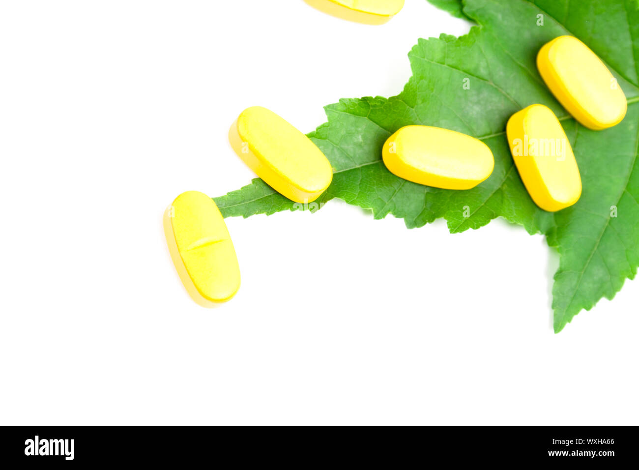 yellow vitamin pills over green leaf on white background Stock Photo