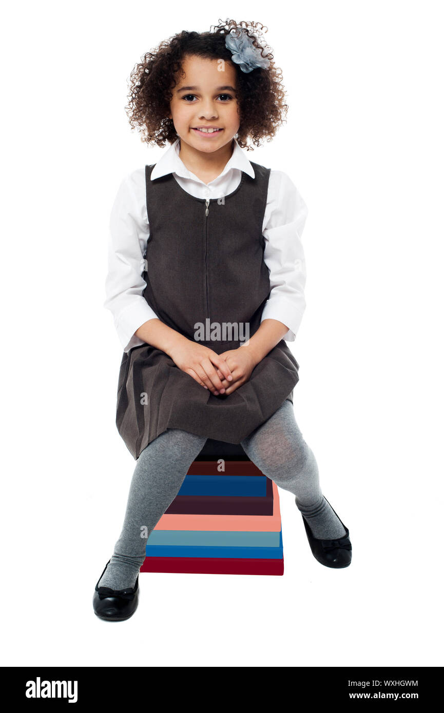 Little school girl sitting on stack of books Stock Photo - Alamy