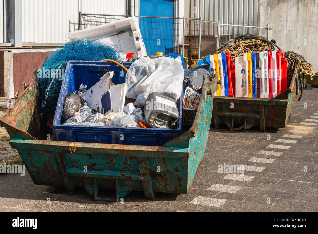 two large steel waste containers filled with plastic bins and plastic fish crates Stock Photo