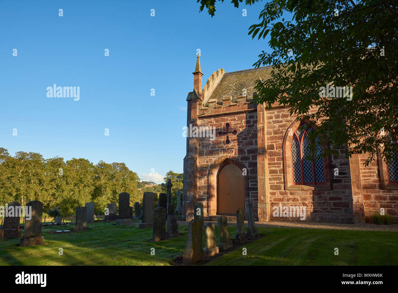 Farnell Parish Church set on a small hill within a Cemetery with the setting sun playing on the red sandstone walls, and creating shadows on the grass Stock Photo