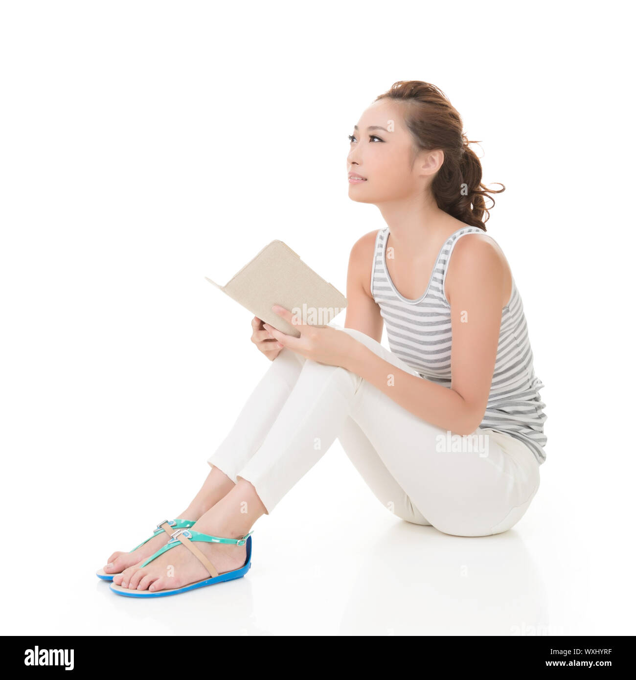 Young woman sit on ground and read a book, full length portrait isolated on white background. Stock Photo