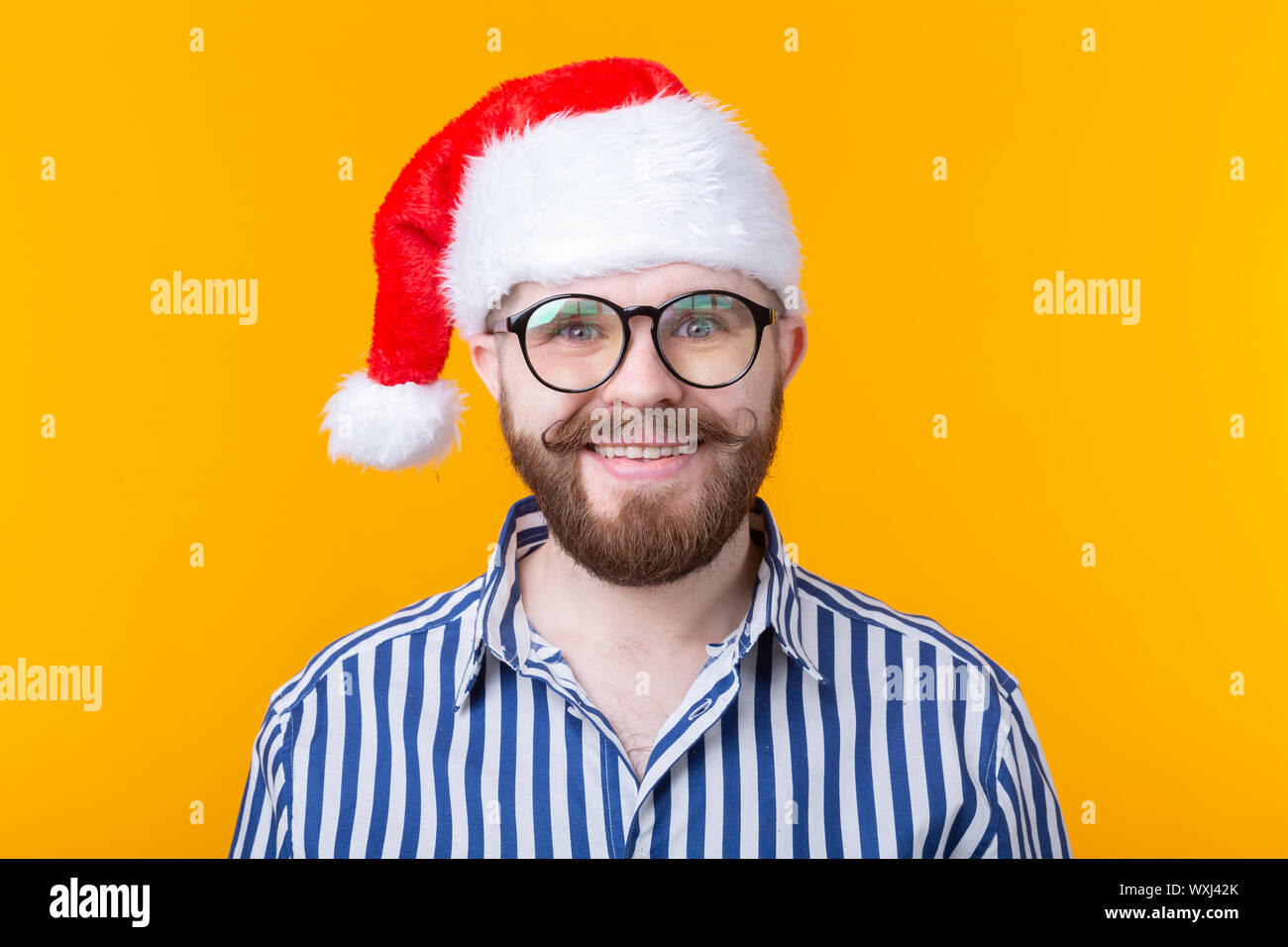 Joyful crazy cute young hipster male in red santa claus hat posing over ...