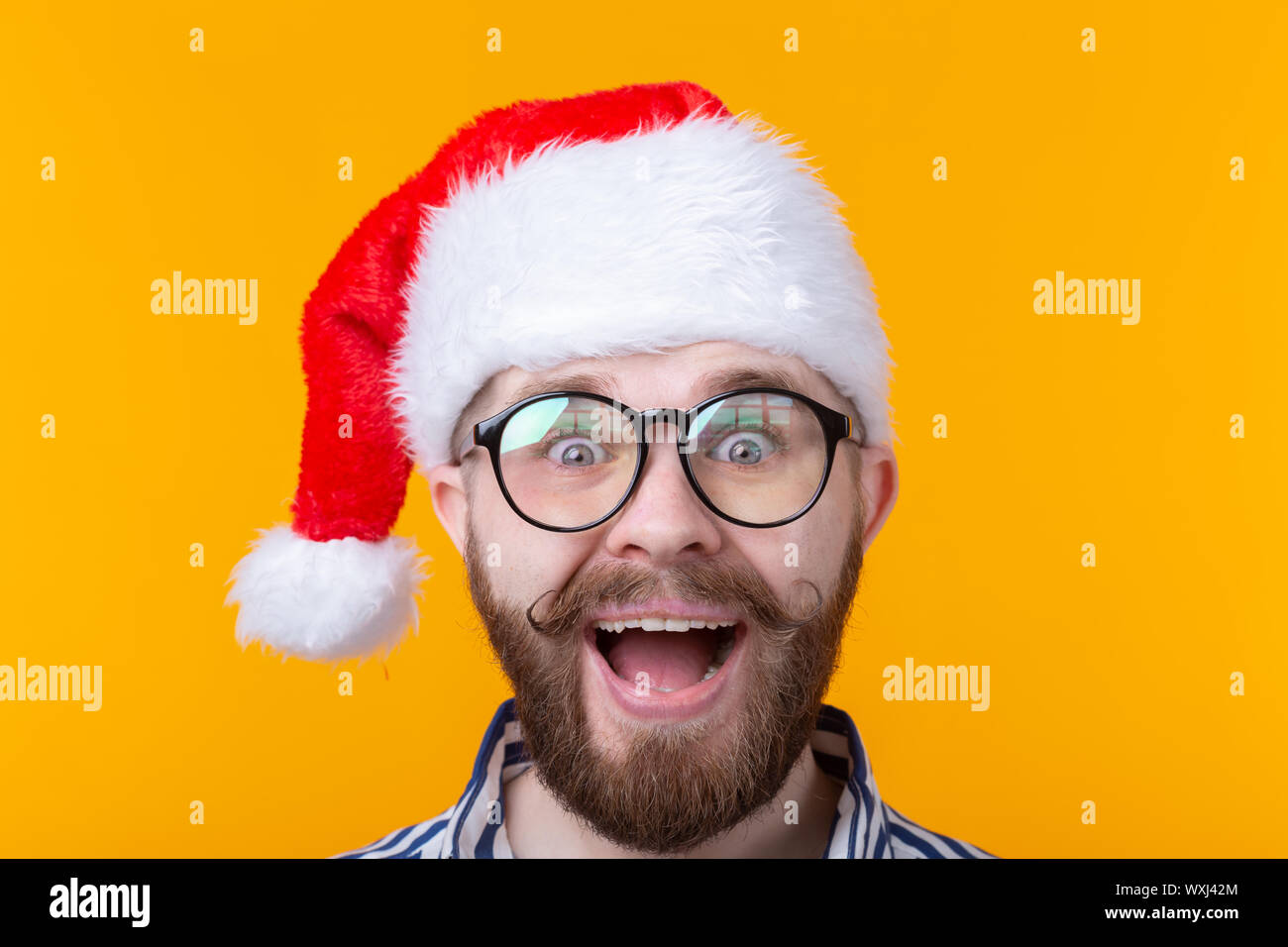 Joyful crazy cute young hipster male in red santa claus hat posing over ...