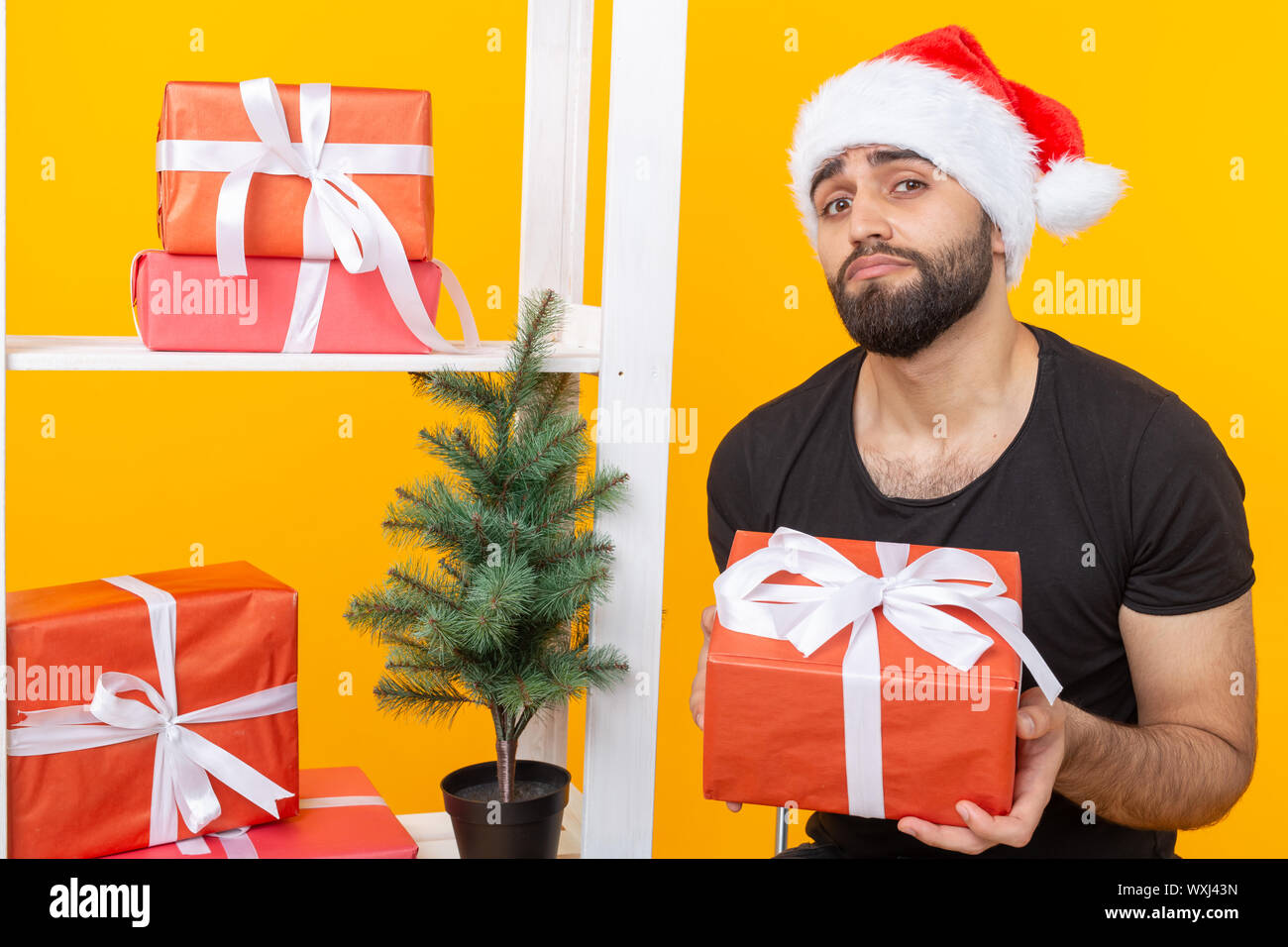 Young handsome man in a Santa Claus hat is holding congratulatory gifts ...