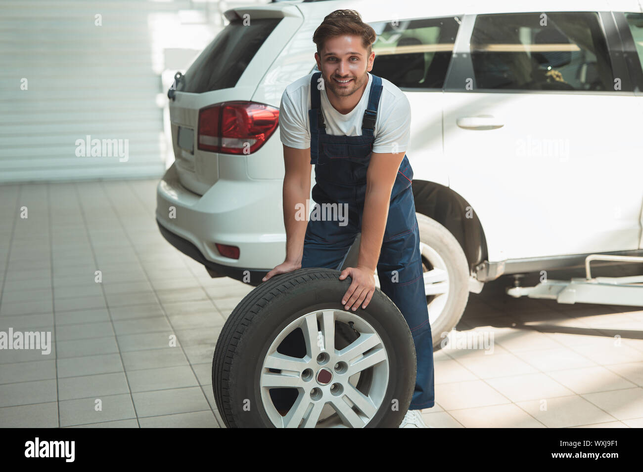young handsome mechanic working in car service department fixing tire . Stock Photo