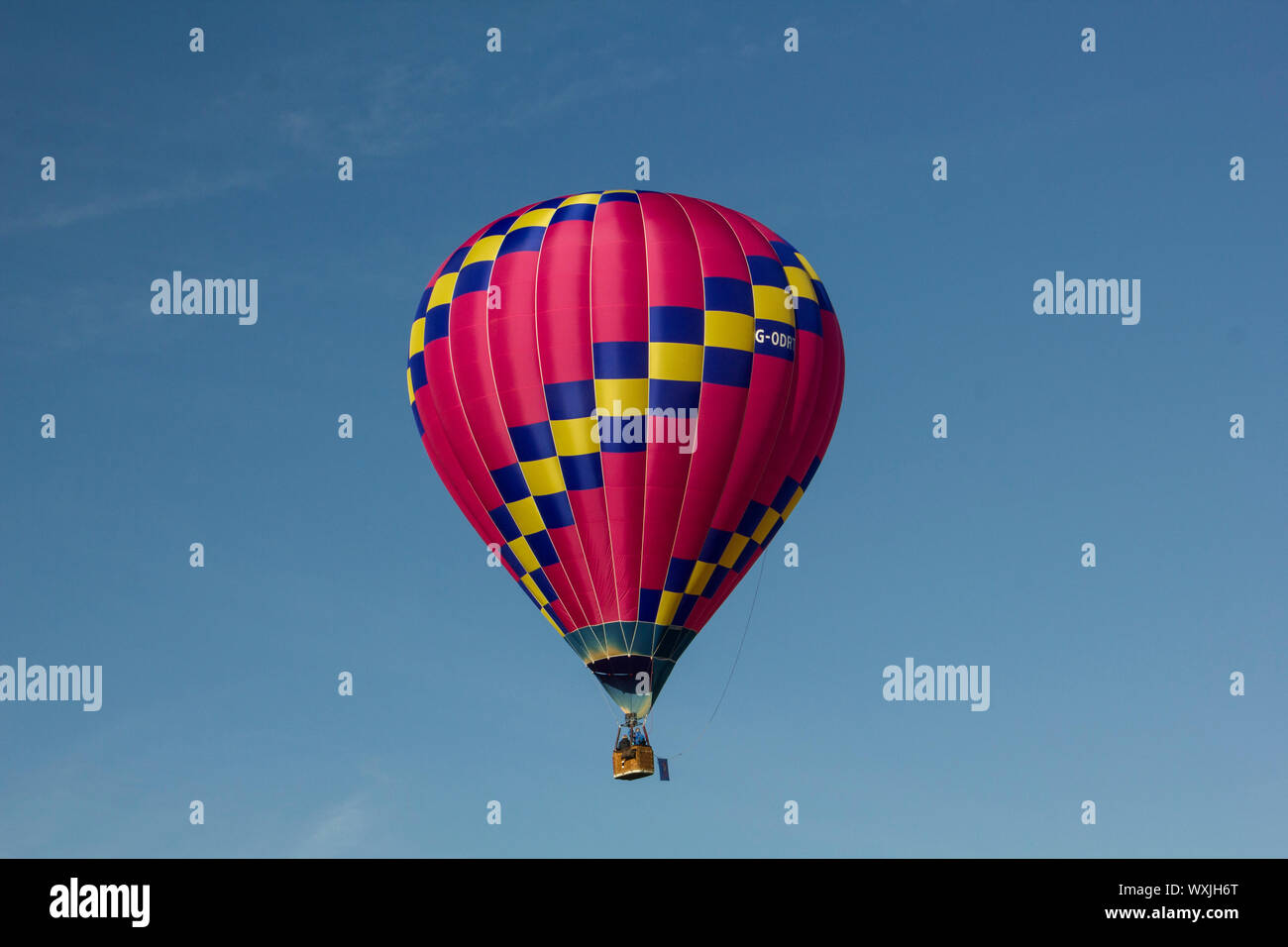 A perfect hot pink with a yellow stripe hot air balloon, flying against a blue sky. Landscape Stock Photo