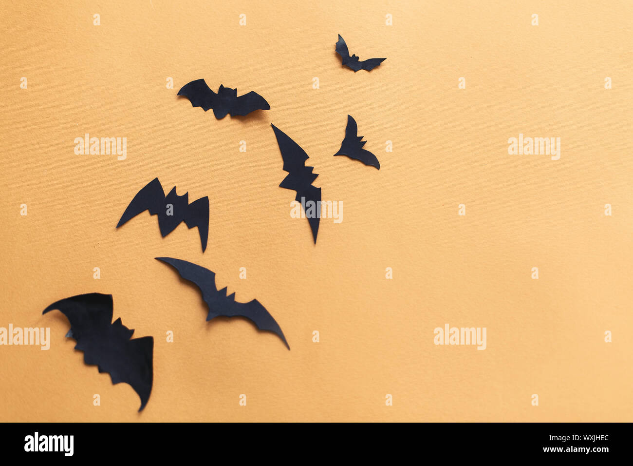 Halloween flat lay. Black paper bats flying on yellow paper background, copy space. Modern spooky halloween decorations. Minimalistic flat lay Stock Photo