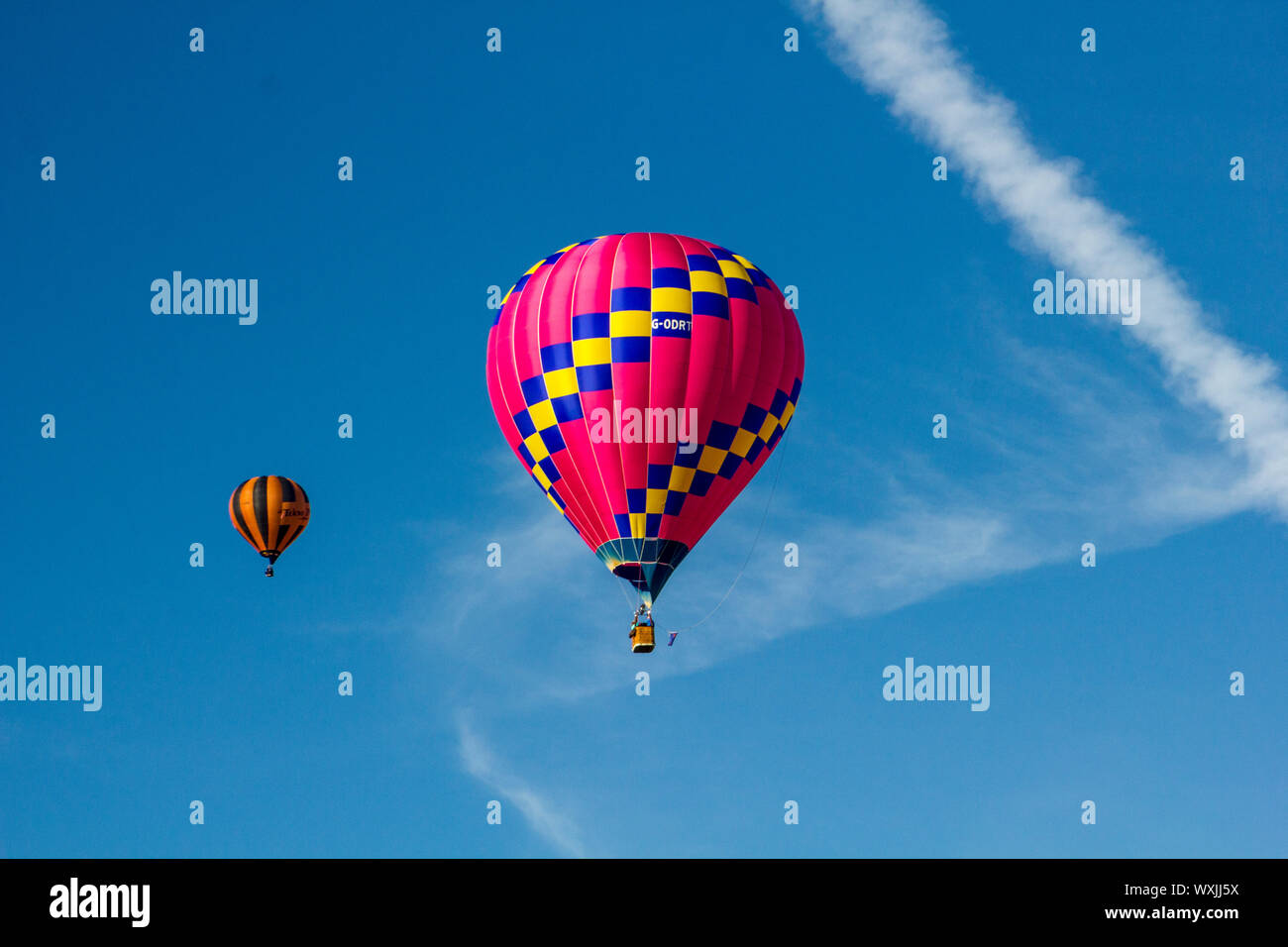 A perfect hot pink with a yellow stripe hot air balloon, flying against a blue sky and a swish of a cloud. Another balloon in the distant background. Stock Photo