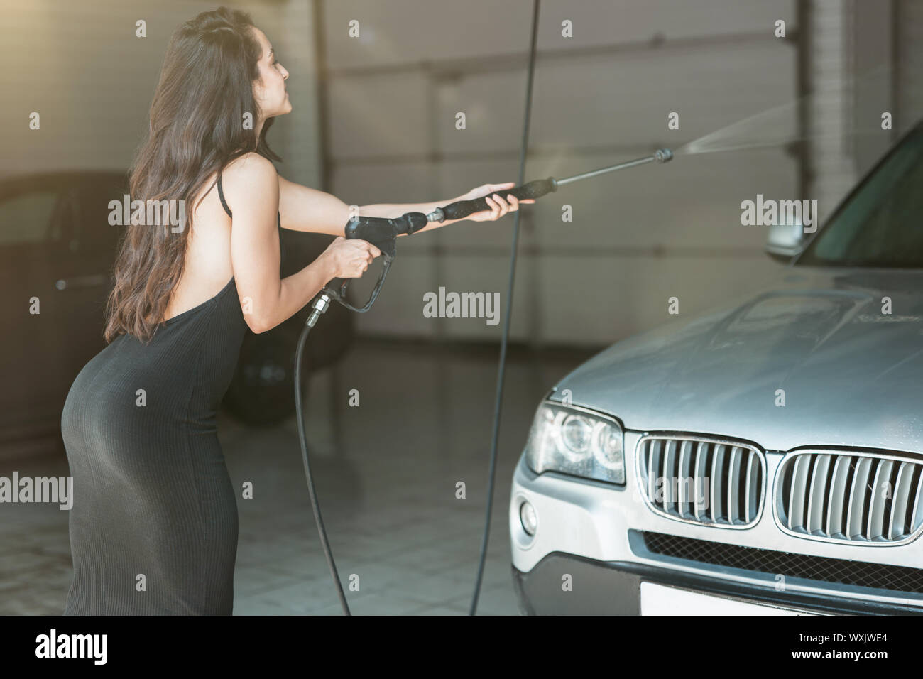 young beautiful woman in black dress washing car at car washing station  using high pressure water looks sexy Stock Photo - Alamy