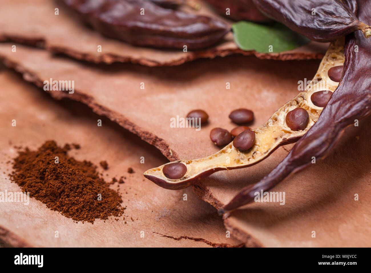 Carob. Organic carob pods with seeds and leaves on tree bark table