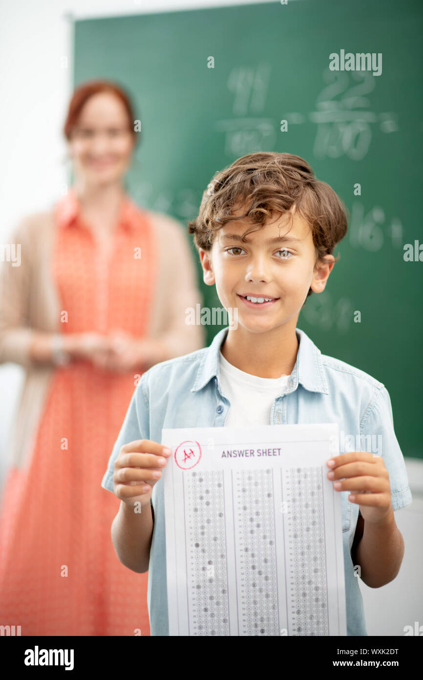 Dark-haired boy standing near blackboard with answer sheet Stock Photo