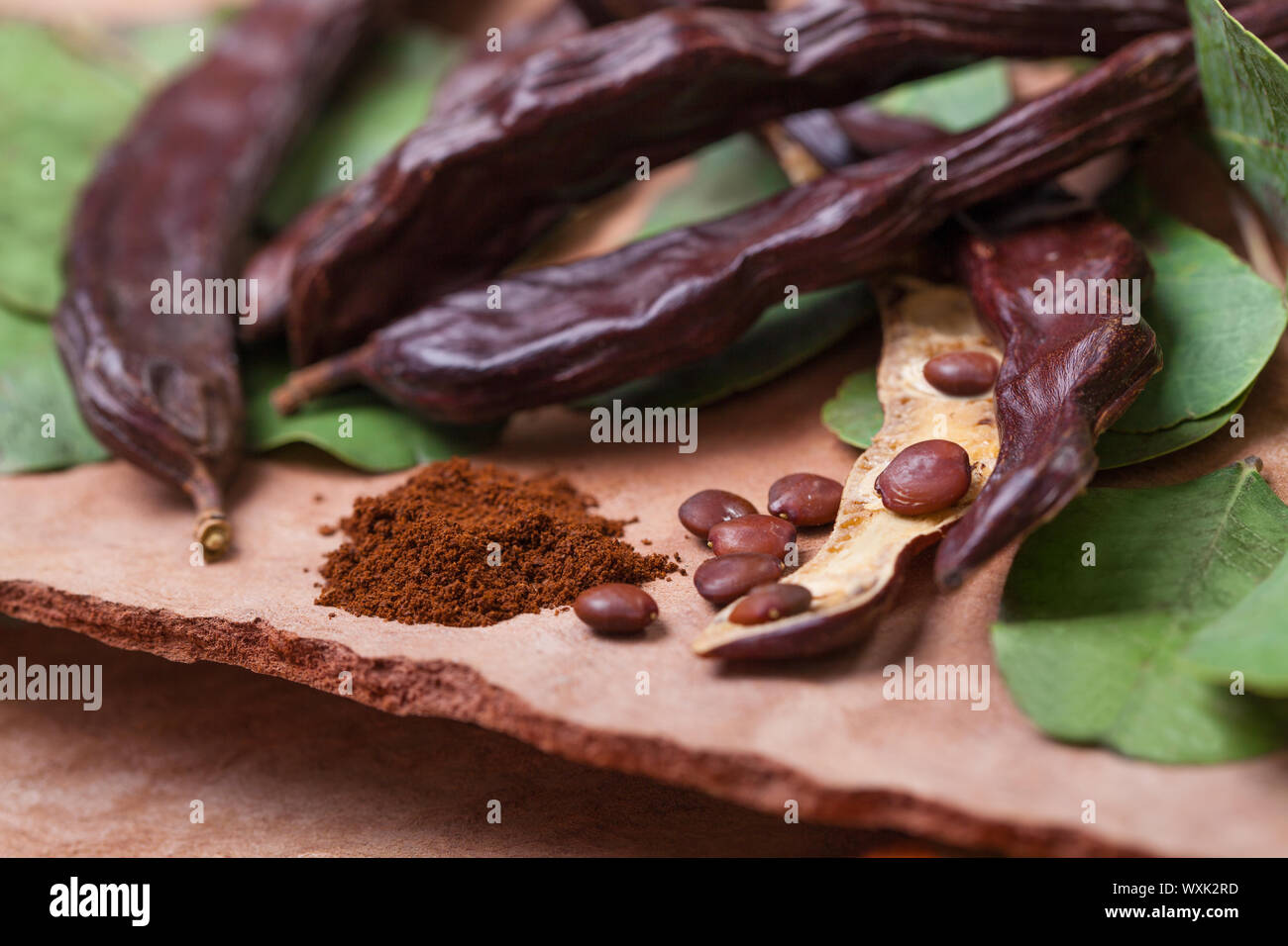 Carob. Organic carob pods with seeds and leaves on tree bark table