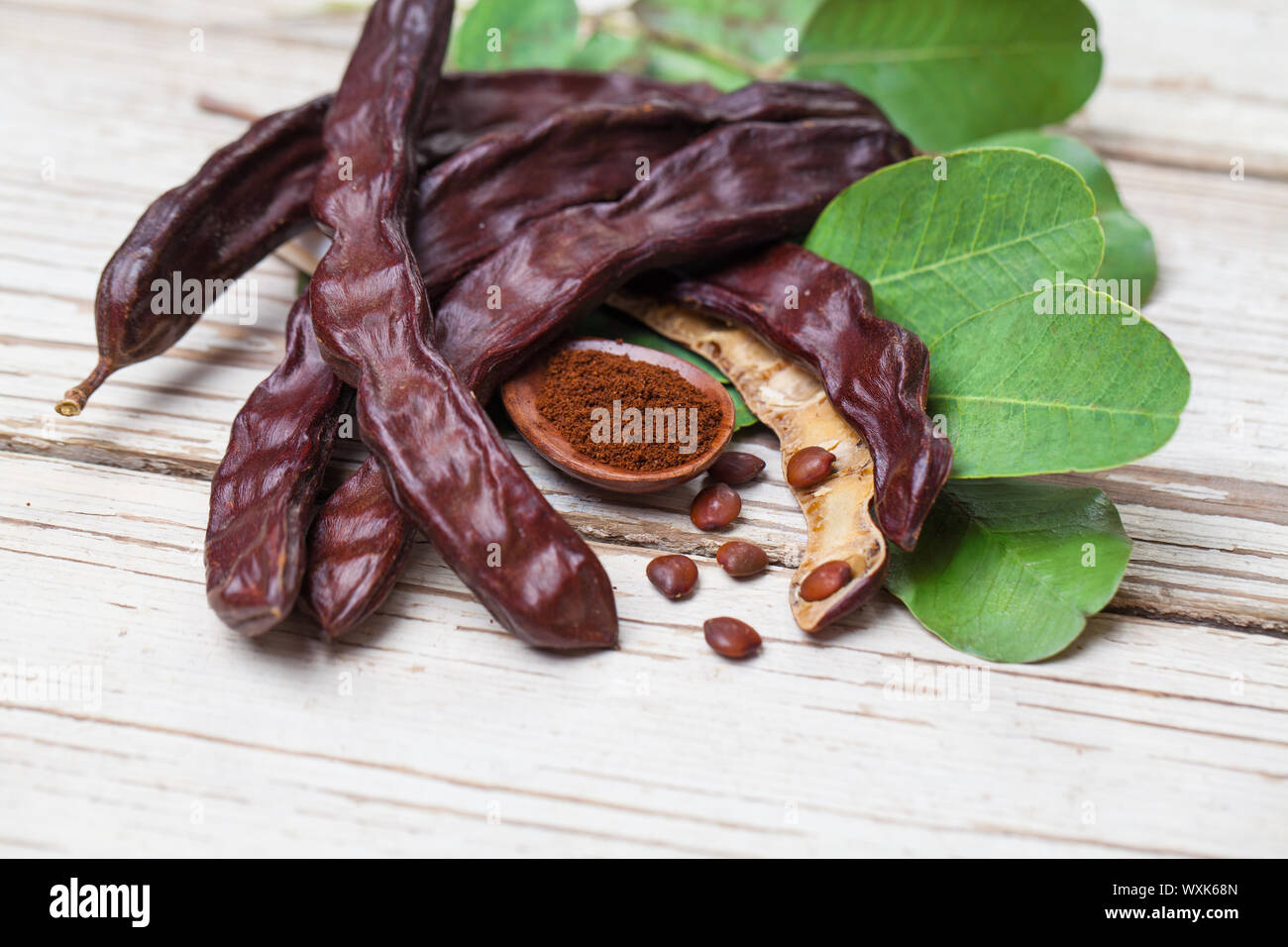 Carob with powder. Organic carob pods with seeds and leaves on white