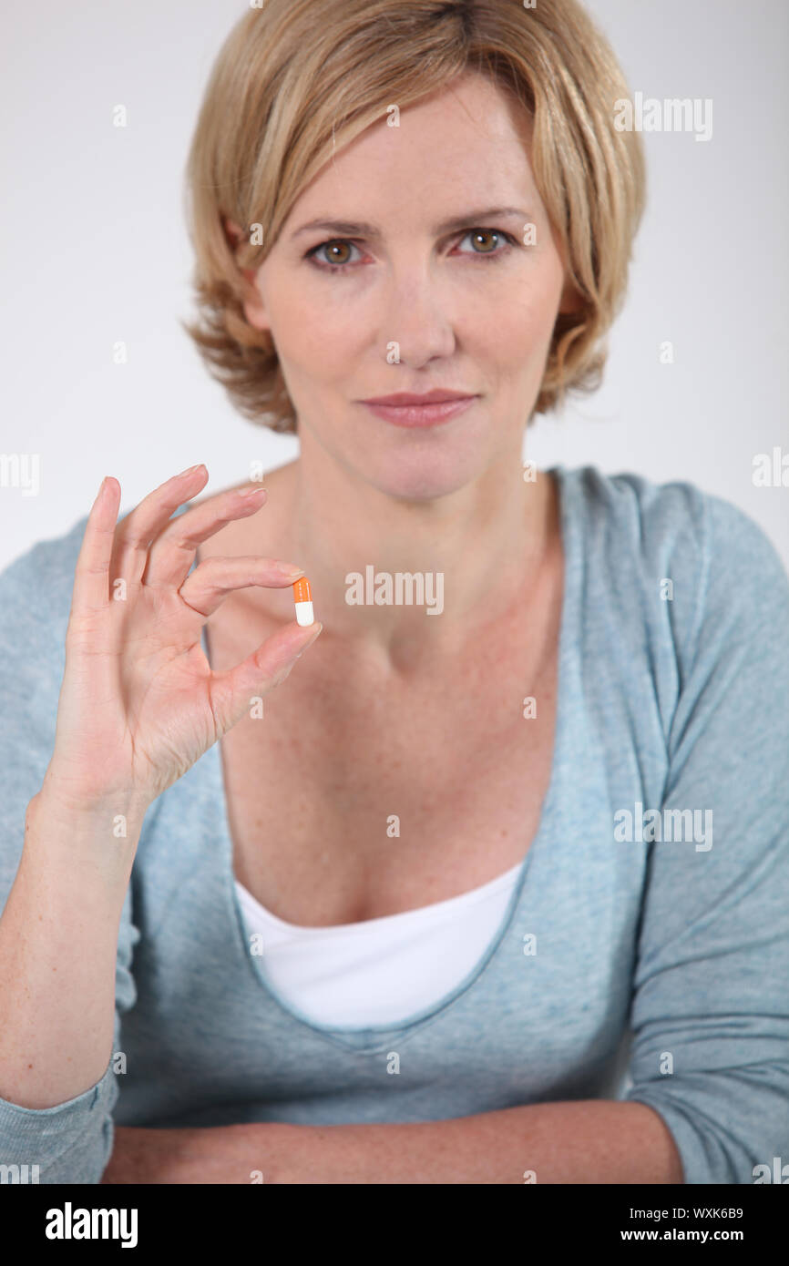 Woman holding a small orange and white capsule of medicine stock photo