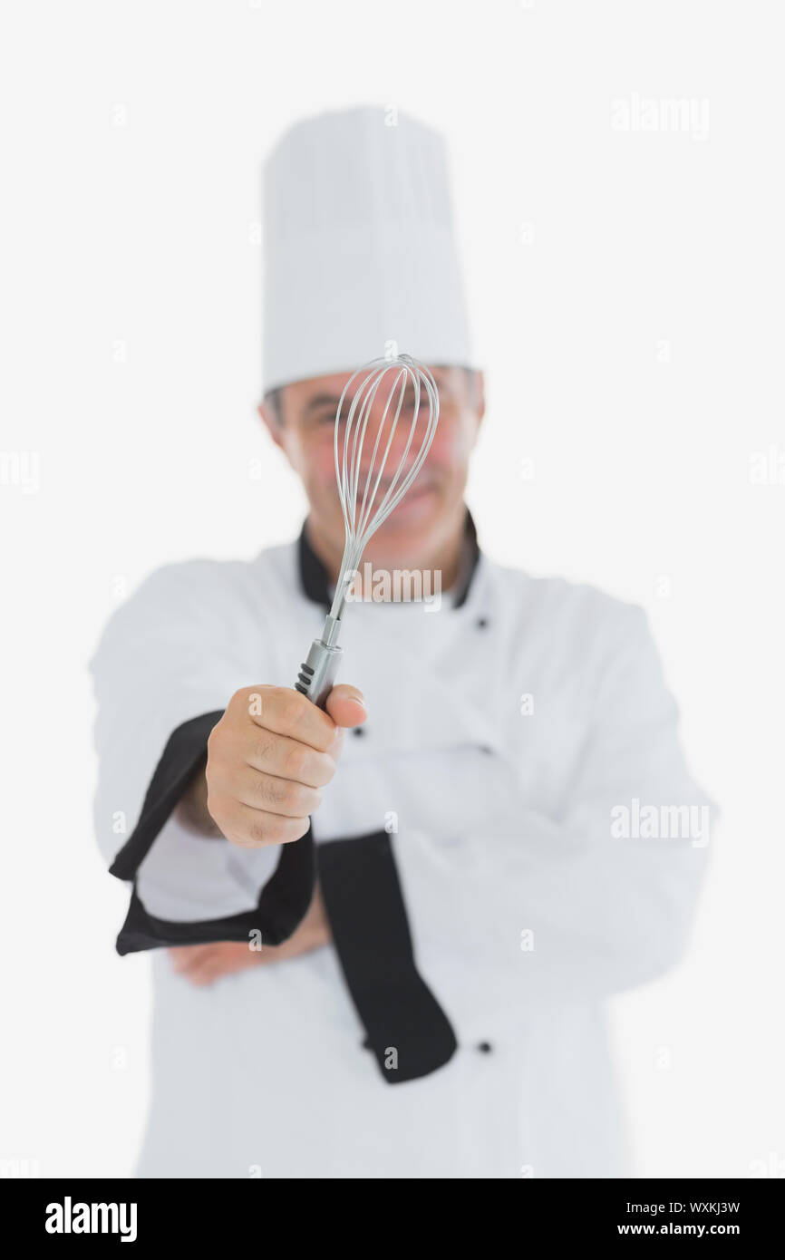 Mature chef showing wire whisk over white background Stock Photo - Alamy