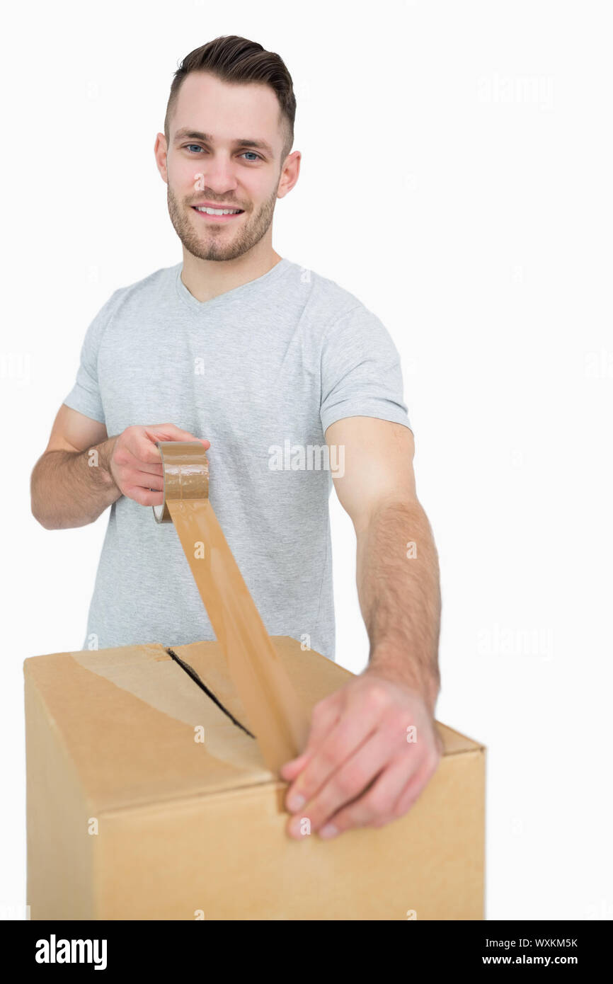 Portrait of young man sealing cardboard box with packing tape over