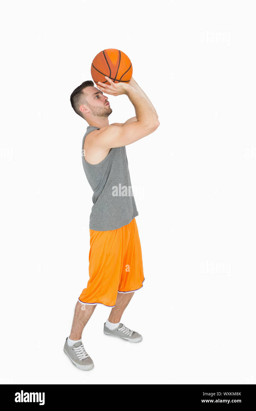 Side view of a young man throwing basketball over white background