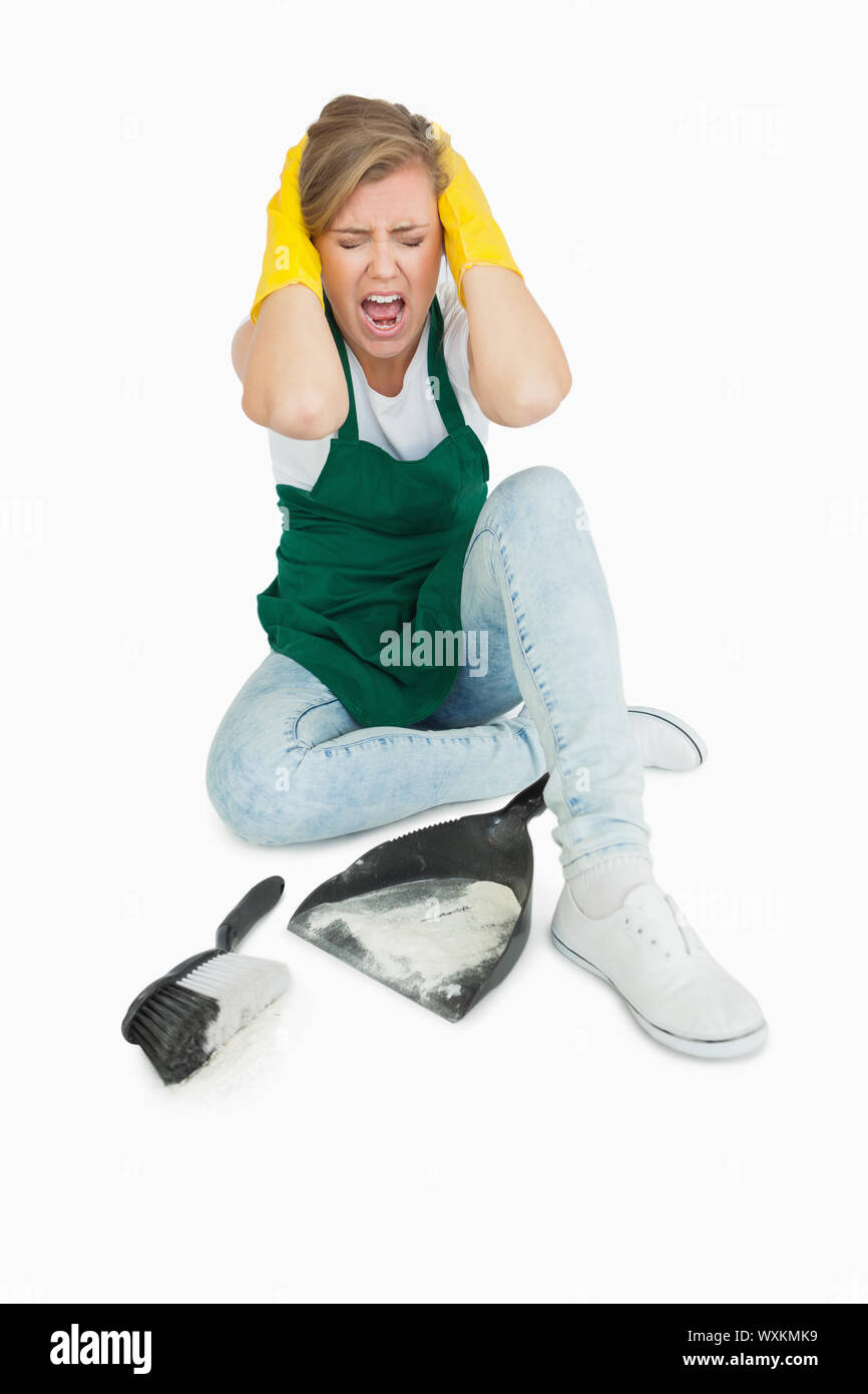 Tired maid screaming as she sits with brush and dust pan over white background Stock Photo