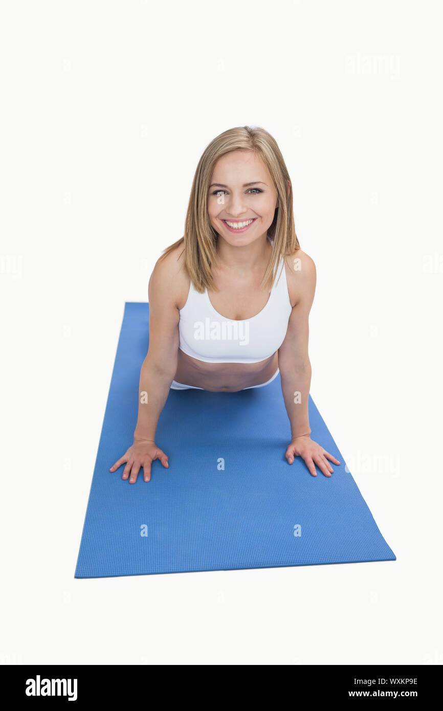 Portrait of happy young woman doing pushups on exercise mat over white background Stock Photo