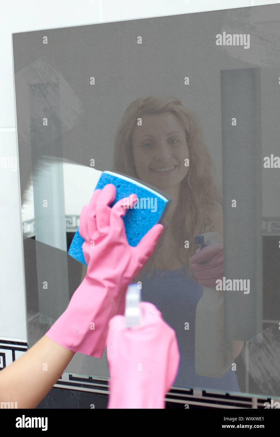 Smiling oman wiping dirt from bathroom mirror using sponge and spray bottle Stock Photo