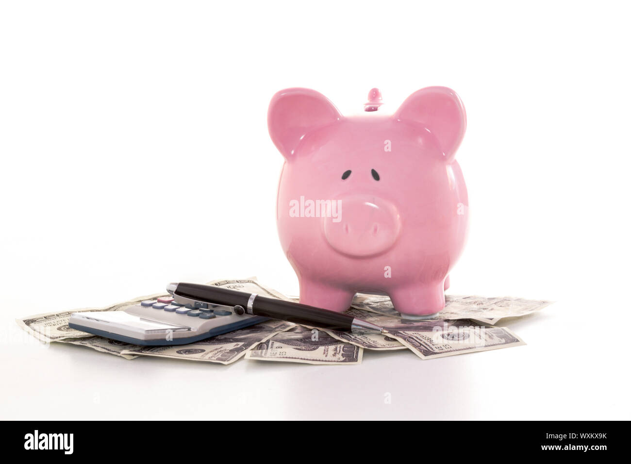 Pink piggy bank beside calculator and fountain pen on white background ...