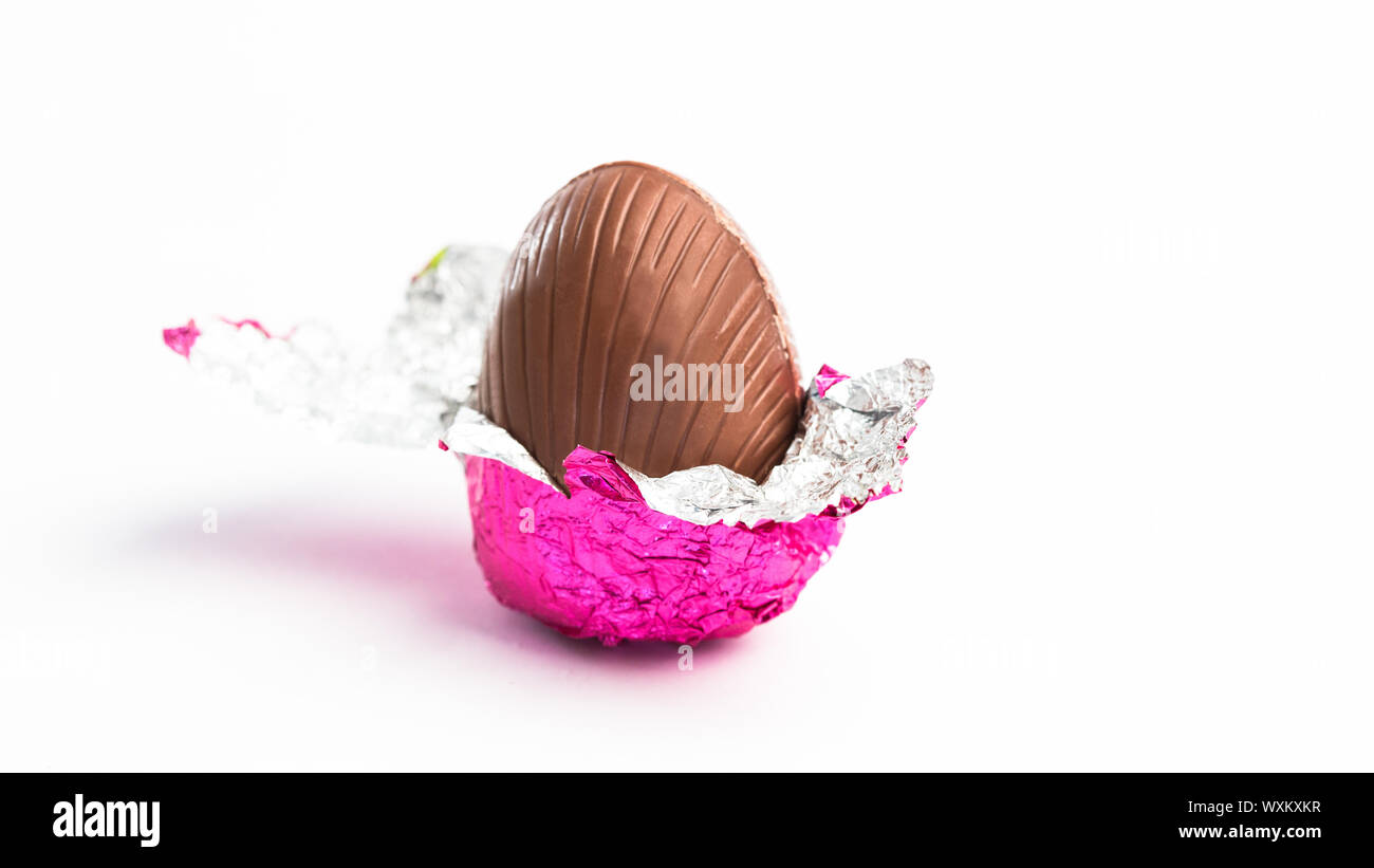 Easter egg unwrapped in pink foil on white background Stock Photo