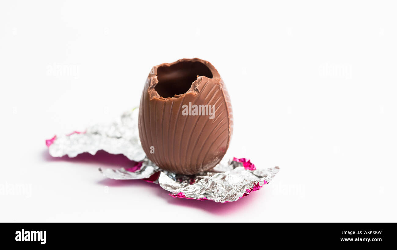 Easter egg unwrapped in pink foil with bite taken out on white background Stock Photo