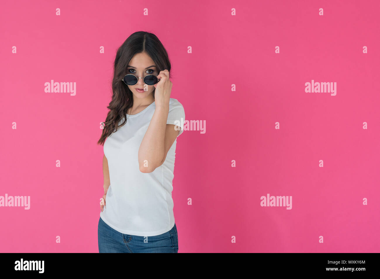 Portrait of a slender brunette in a white t-shirt on a pink background. Mock-up for t-shirt design Stock Photo