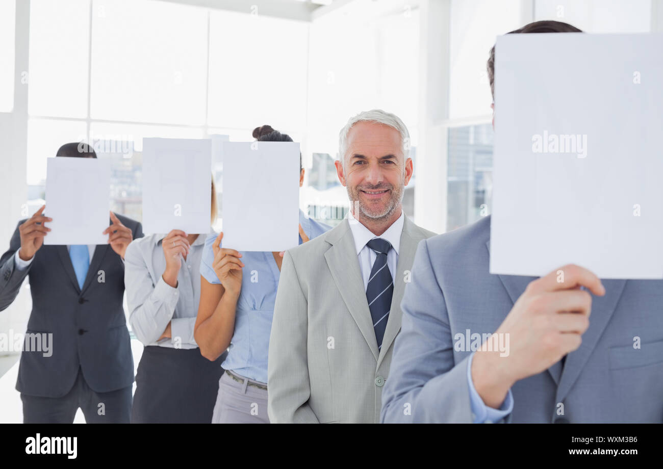 Business team covering face with white paper except for one smiling at camera Stock Photo