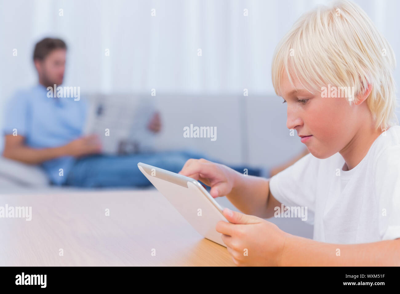 Boy using tablet while his father is reading on the couch Stock Photo