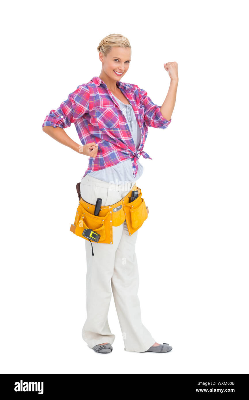 Happy blonde woman tensing arms wearing tool belt on white background ...