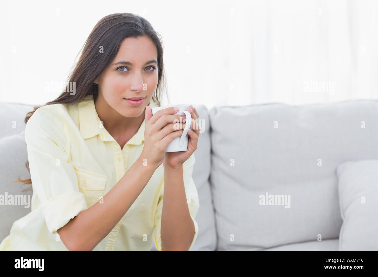 Portrait of a woman holding a cup of coffee sat on a couch Stock Photo ...