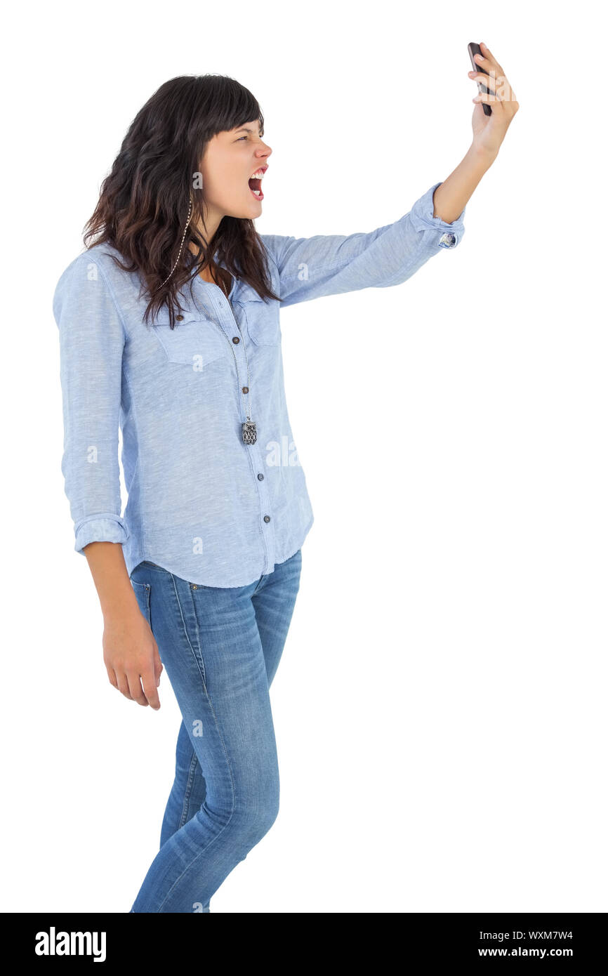 Furious brunette holding her mobile phone and screaming on white background Stock Photo