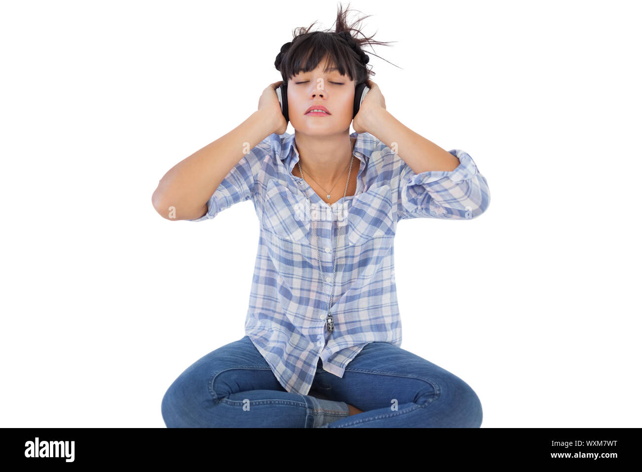 Young woman sitting on the floor listening to music on white background ...