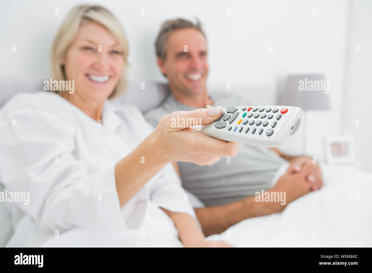 Smiling couple watching tv in bed at home in bedroom Stock Photo Alamy