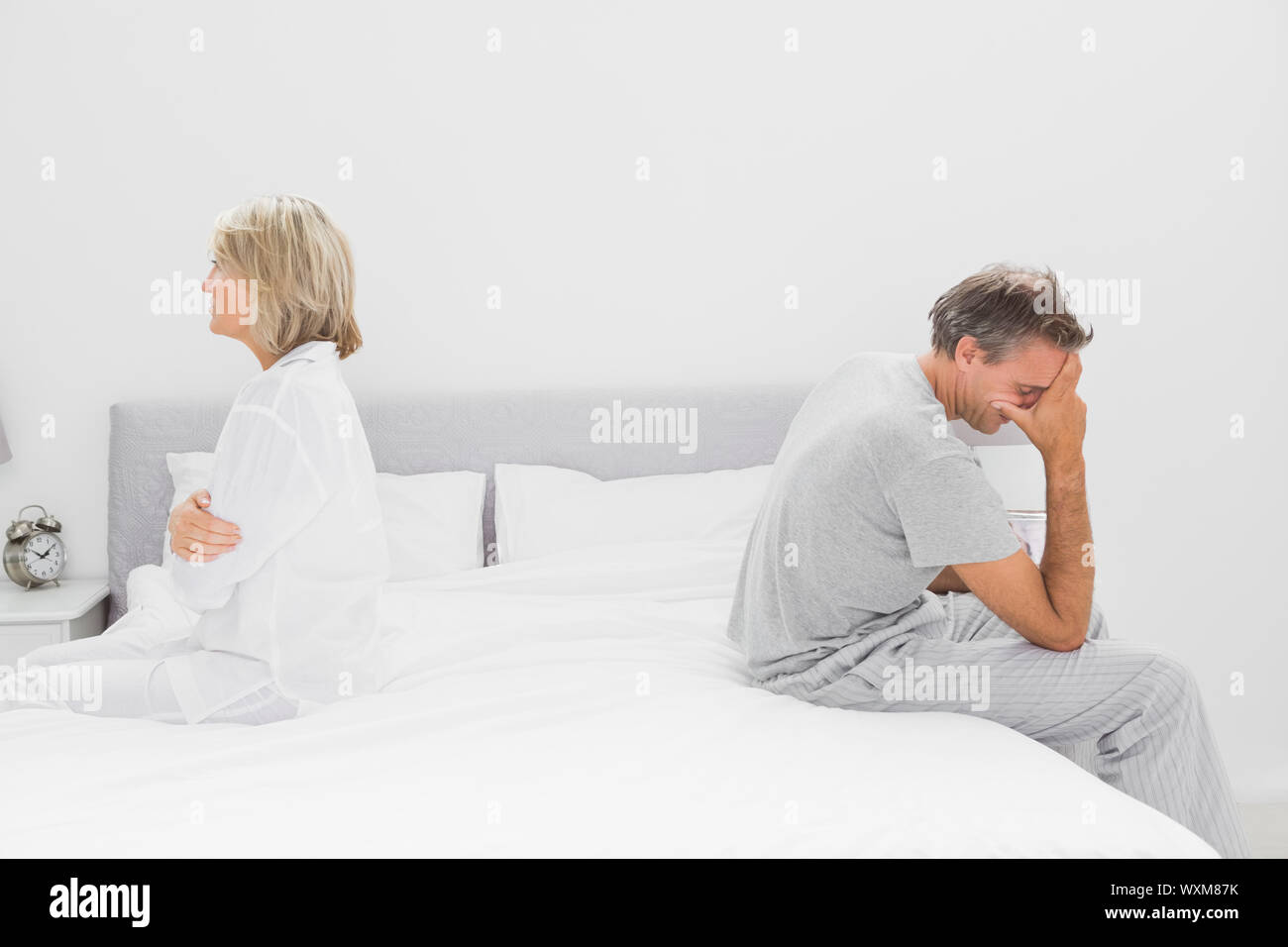 Couple sitting on opposite sides of bed after a dispute Stock Photo - Alamy