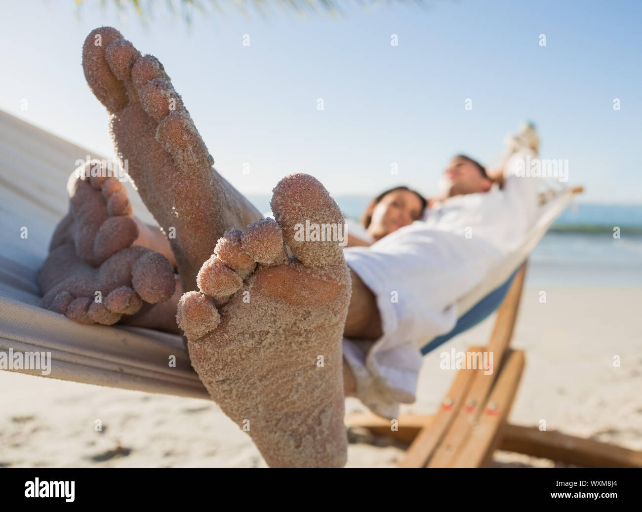 Close up of sandy feet of couple in a hammock on the beach Stock