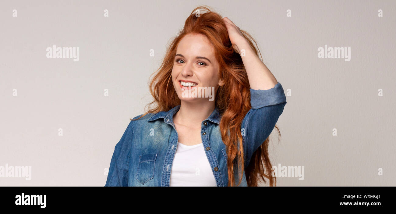 Beautiful young girl touching her curly ginger hair and smiling Stock Photo