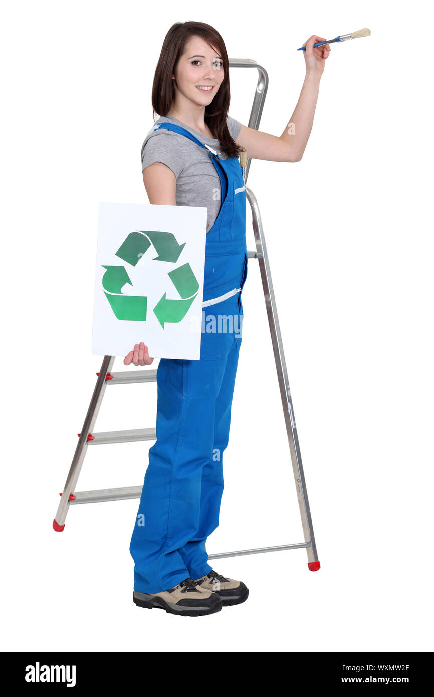 lovely brunet painter in blue dungarees holding brush and recycling logo Stock Photo