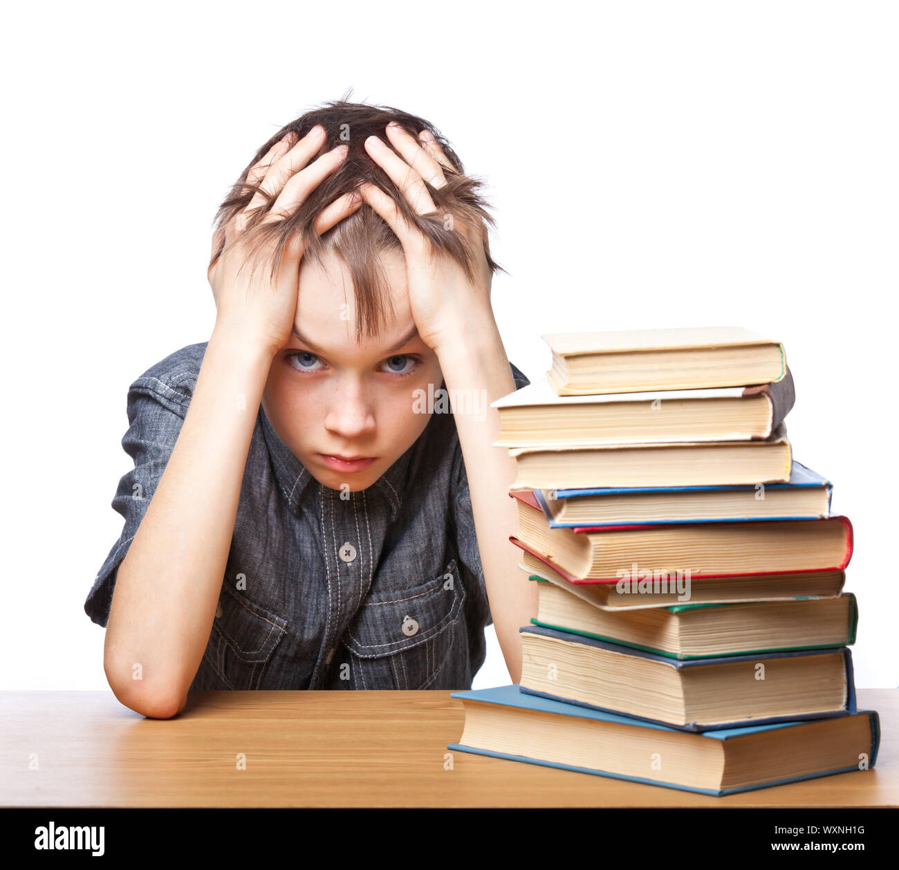Portrait of upset schoolboy sitting at desk with books holding his head Stock Photo